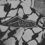Black and white close-up of a keffiyeh scarf with a Palestine map pendant